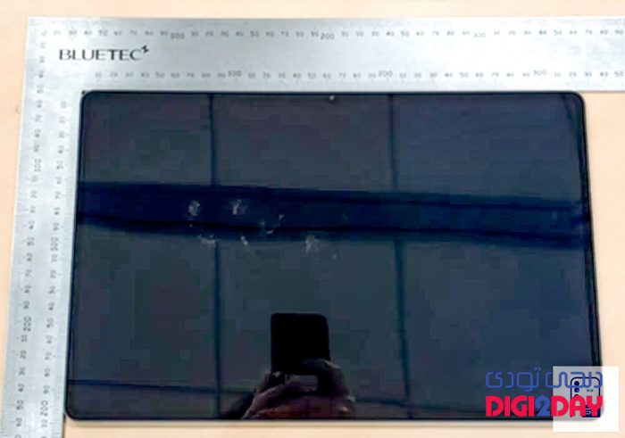 Top-down view of a dark smartphone on a light desk, with metal rulers along the top and left edges and a 5G sticker in the bottom-right corner.